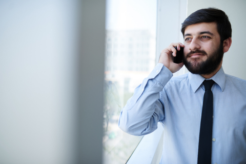 Portrait of smiling businessman standing by window and calling